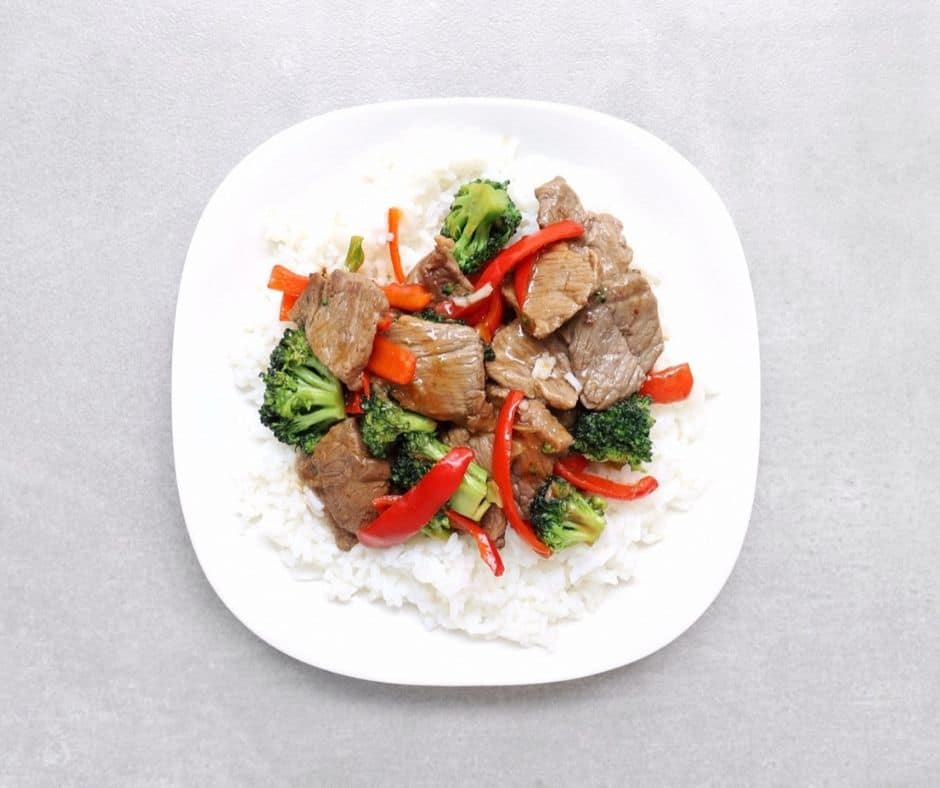 a plate of sesame beef stir fry with broccoli and peppers